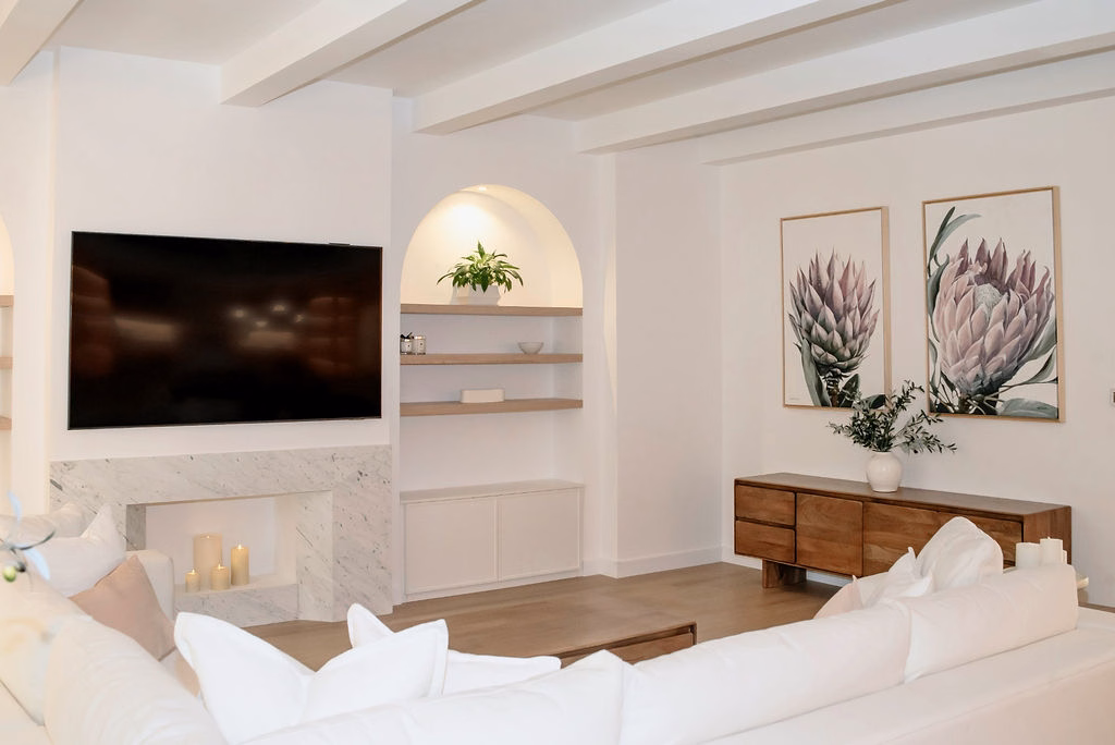 Living room seating layout showcasing a plush white sectional couch, wall-mounted television, marble fireplace surround, and decorative arched wall niches.